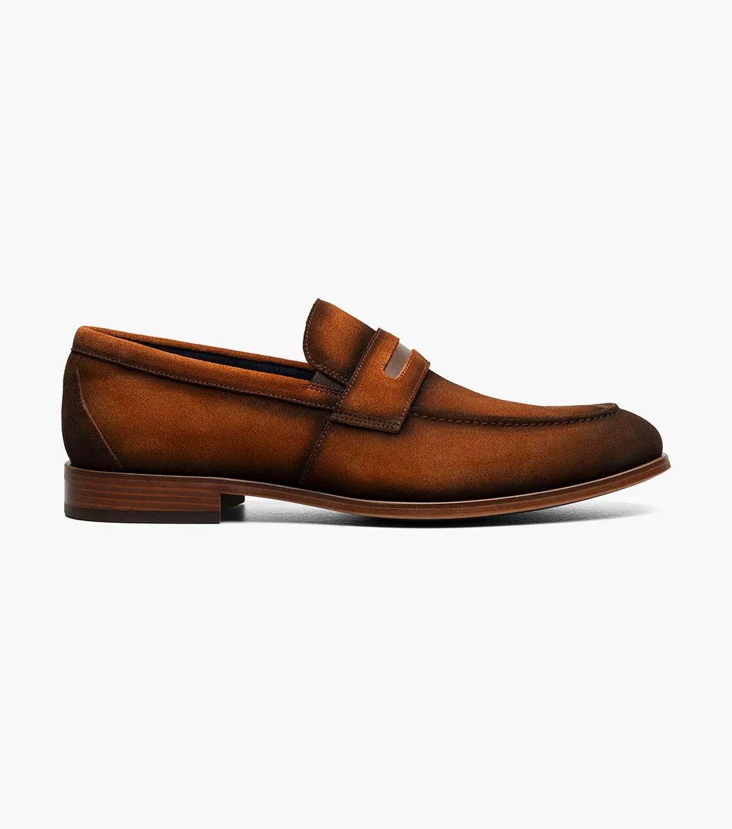 The STACY ADAMS Burke Moc Toe Saddle Slip On in copper (25676-220) features brown suede, a leather strap detail, stitching accents, a low wooden heel, and a cushioned footbed for comfort, shown on a white background.