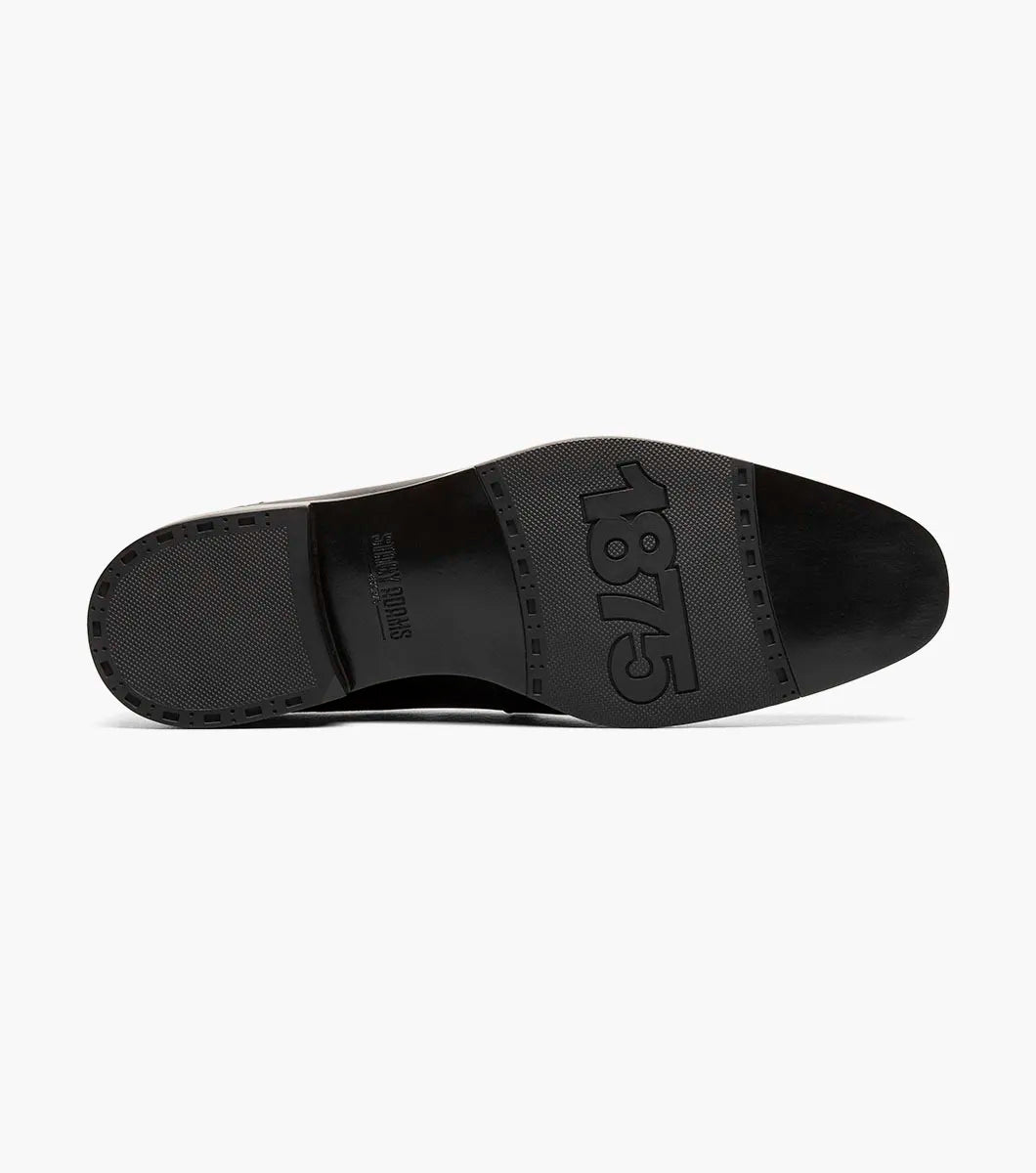 The Stacy Adams Aiden Moc Toe Slip On (25655-001) in black features a genuine leather upper with textured perforation, anatomical arch support, and a low heel. Displayed on a white background.