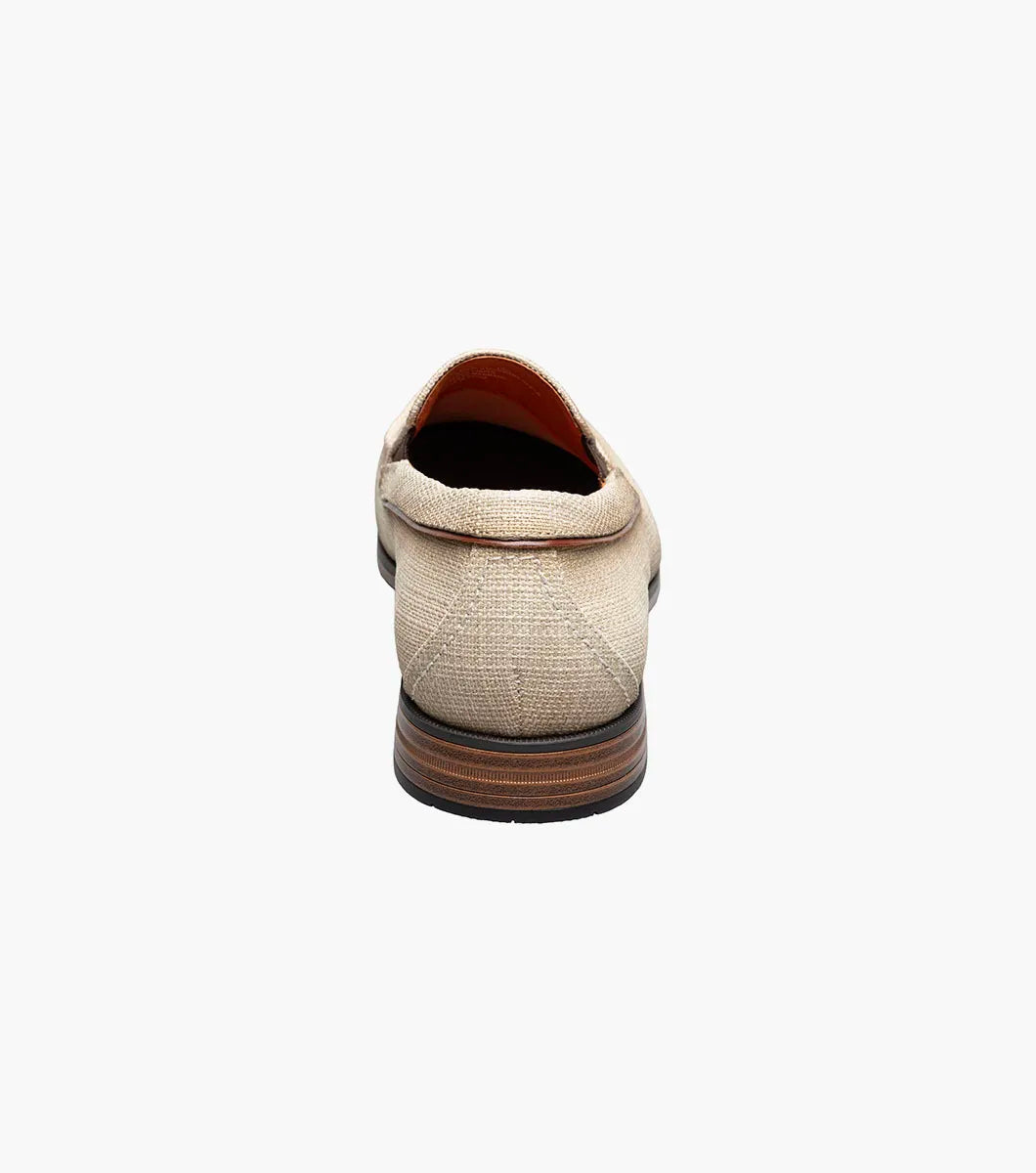 The Stacy Adams Ridgely Moc Toe Slip On (Natural) features a textured fabric upper, brown trim, anatomical arch support, and a low wooden heel for comfort, shown here on a white background.