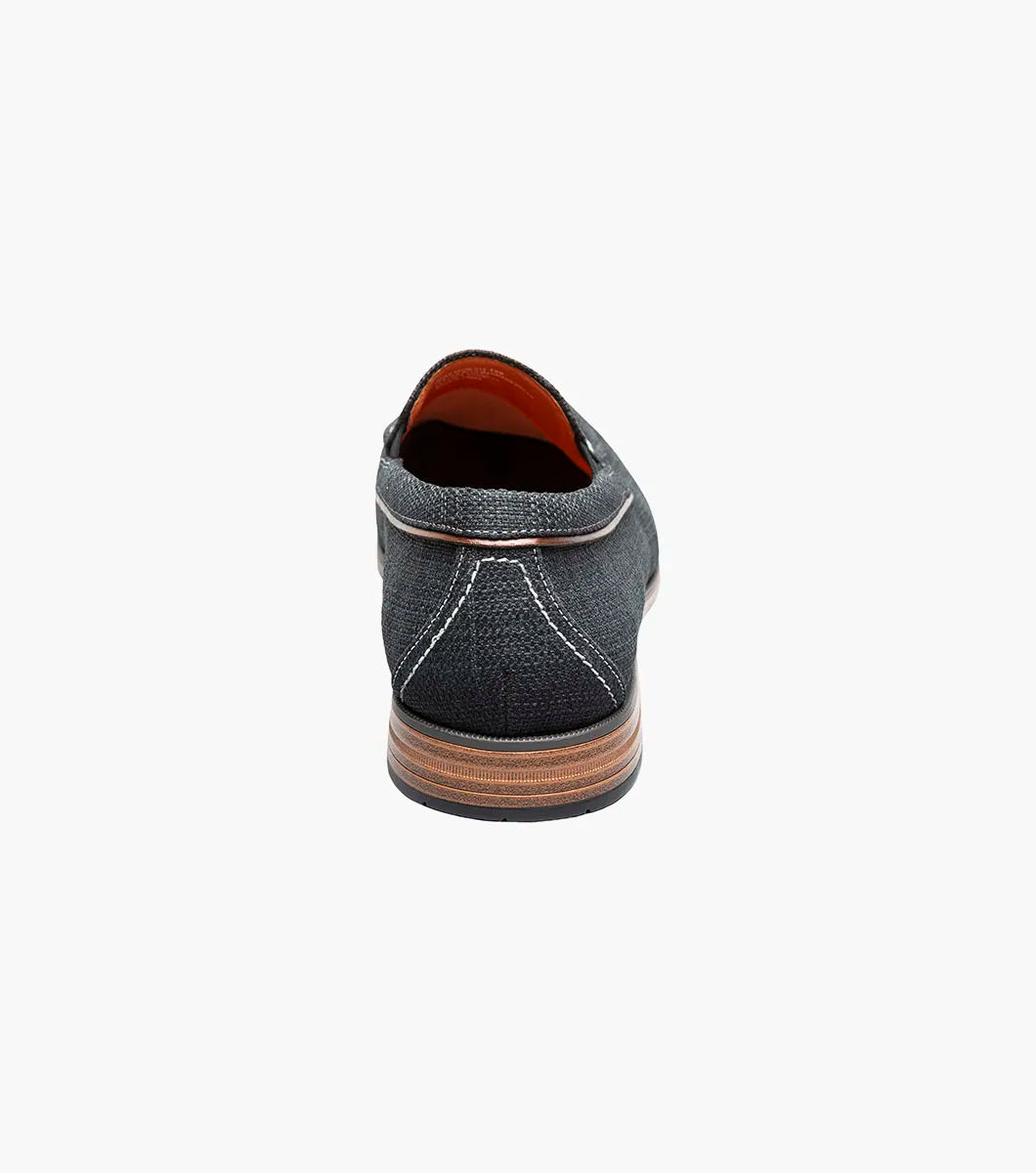 The Stacy Adams Ridgely Moc Toe Slip On in charcoal features visible stitching, a low wooden heel, comfy footbed, and tan lining. Shown against a white background, this casual loafer is perfect for everyday wear.
