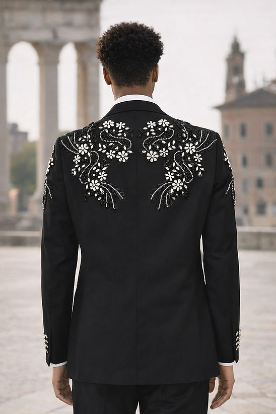 A man in a Manzini GQ300 2-Piece Slim-Fit Men's Rhinestone Pattern Double Breast Tuxedo Suit in black and silver stands by a black car, with historic buildings and stone columns behind him.