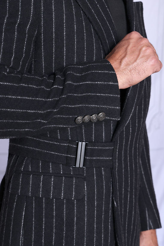 A man wears the Manzini MZW-703 Men's Wool Feel Pinstripe Blazer Coat with Hook Belt in black, standing against a light background and looking slightly to the side.