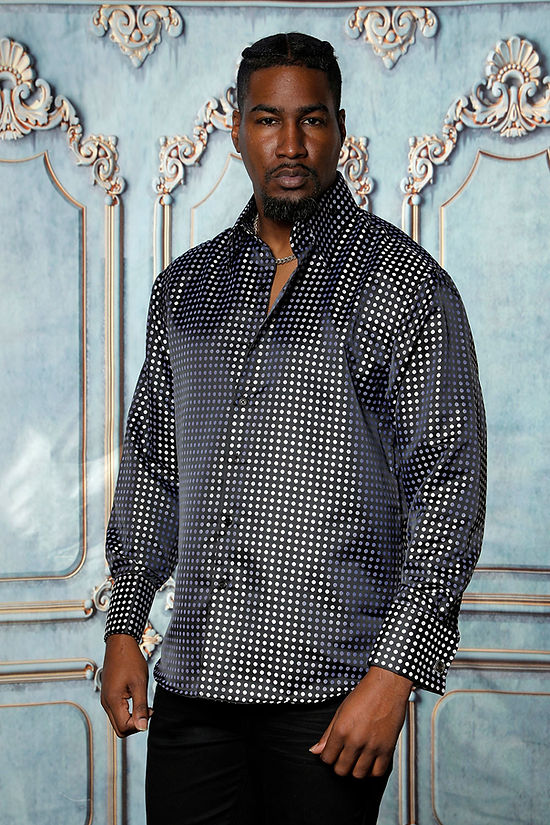 A man stands before an ornate blue and gold wall, wearing the Manzini MANZINI MZT-164 Small Polka Dot Black Long Sleeve Satin Shirt with cuff & link and black pants.