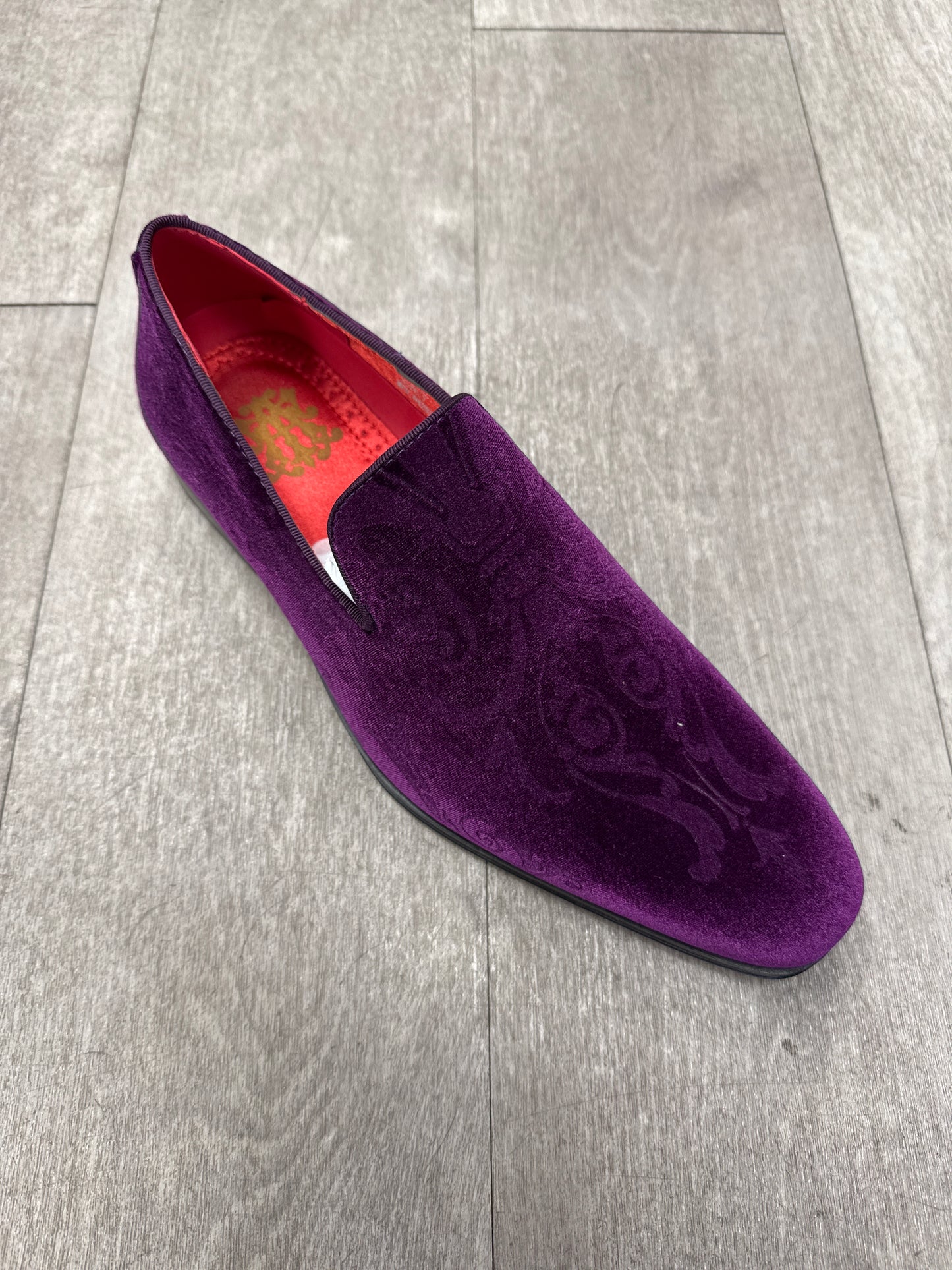 The AFTER MIDNIGHT 7017 PURPLE PAISLEY velvet slip-on, featuring a sleek buckle and subtle side stitching, rests on a wooden floor.