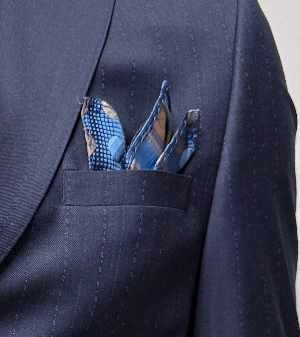 A mannequin dressed in the Tiglio Luxe Dolcetto Modern Fit Navy Fancy Pinstripe Wool Suit TL8107 by Tiglio Luxe, paired with a crisp white dress shirt, a blue polka dot tie, and a coordinating pocket square, posed against a plain light-colored background, exemplifies the refined elegance of tailored men’s clothing.