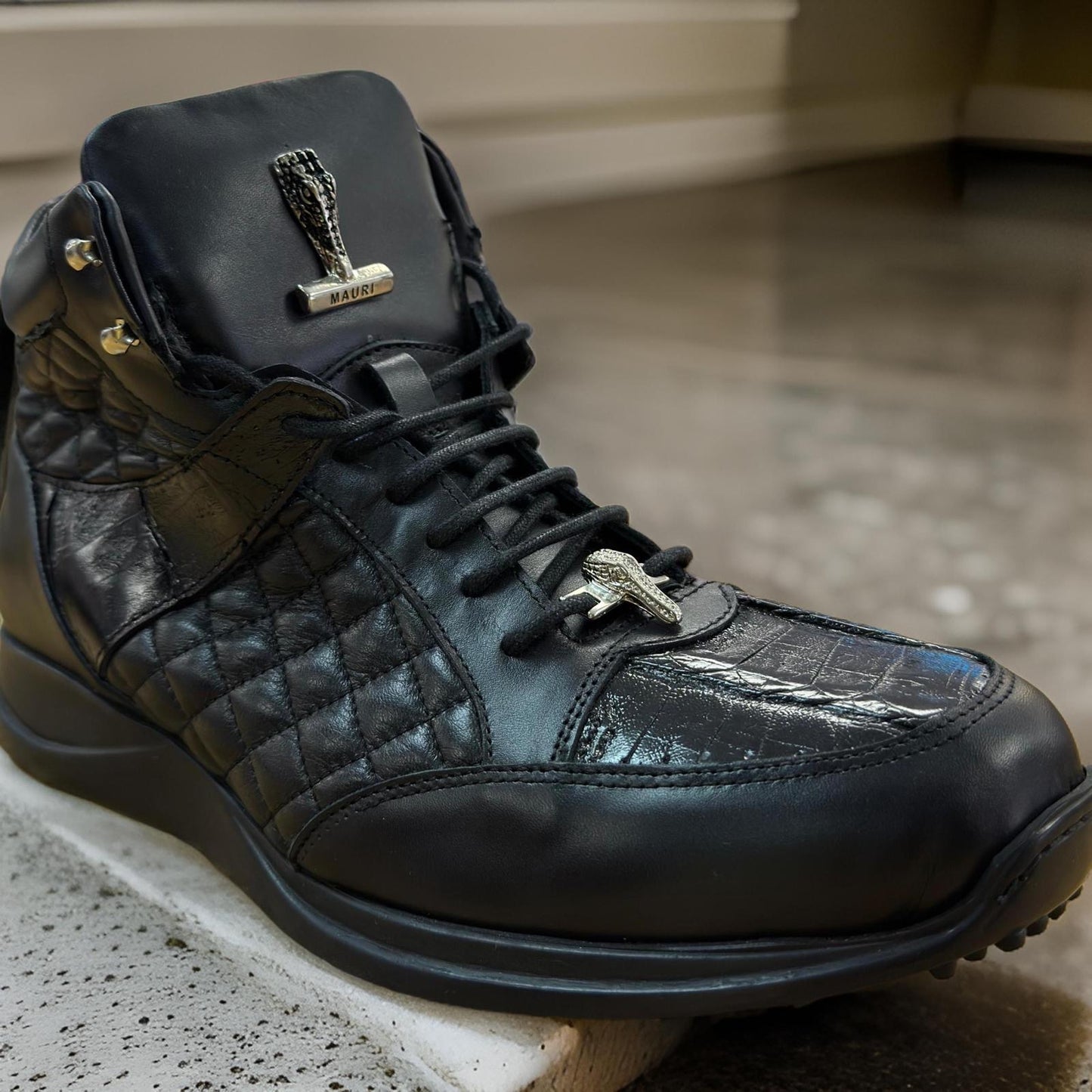 Close-up of the Mauri 8400 Black Boots featuring quilted black leather with textured baby crocodile-like patterns on glossy patent leather, accented by a gold emblem on the tongue and side.