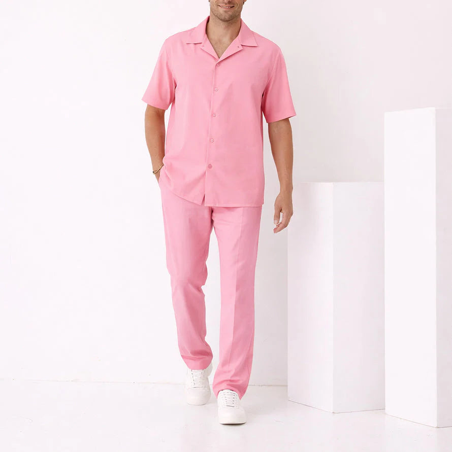 A man stands in a minimalist, white room wearing the Inserch 2pc Set SE9356 Summer Pink—shirt and pants by Inserch—paired with white sneakers.