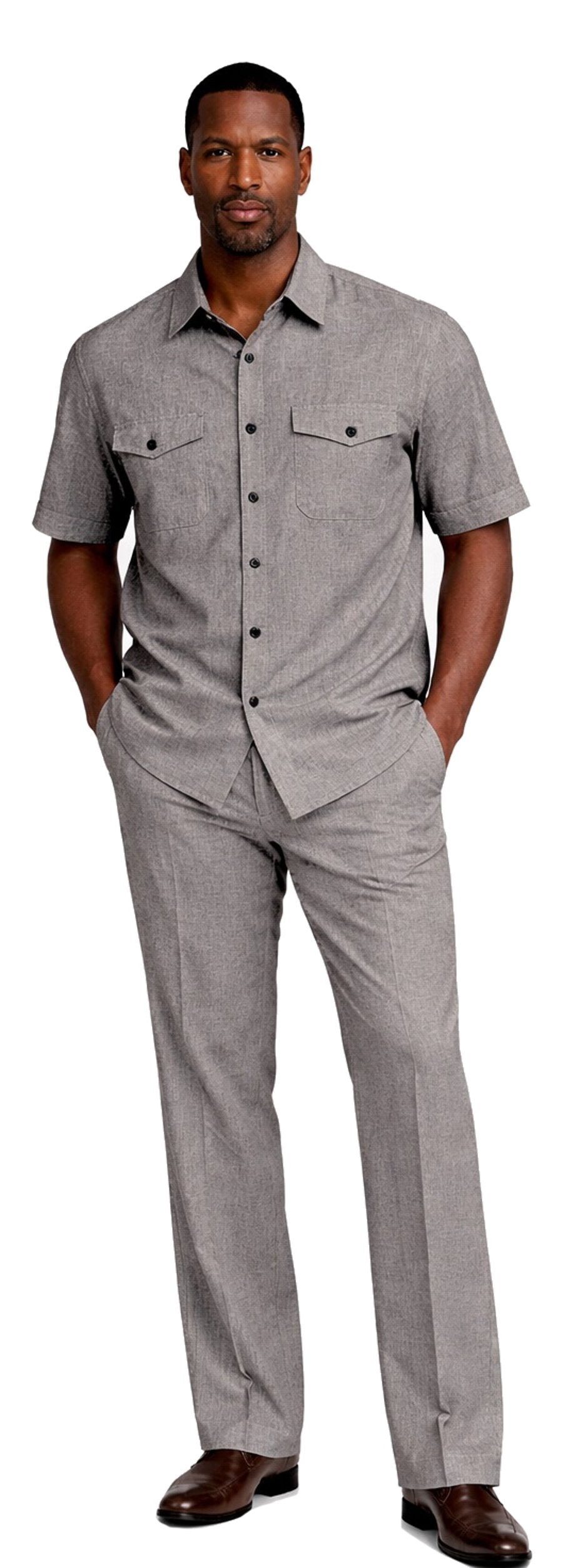A man stands with hands in pockets, wearing the Bassiri Charcoal 2pc Set A 145 by Bassiri—featuring a gray short-sleeve button-up shirt with chest pockets and matching pants—paired with brown shoes.