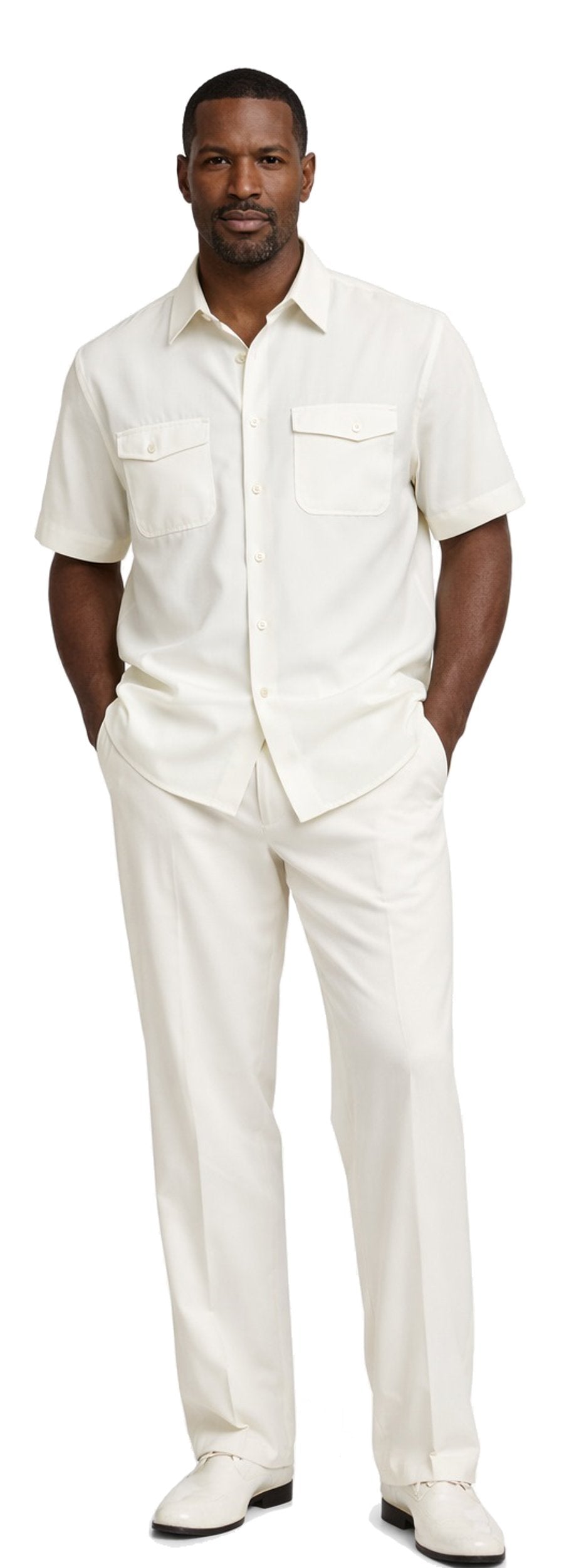 A man wears the Bassiri White 2pc Set A 145 by Bassiri—featuring a short-sleeve, button-up cream shirt with two chest pockets, matching cream trousers, and cream shoes.