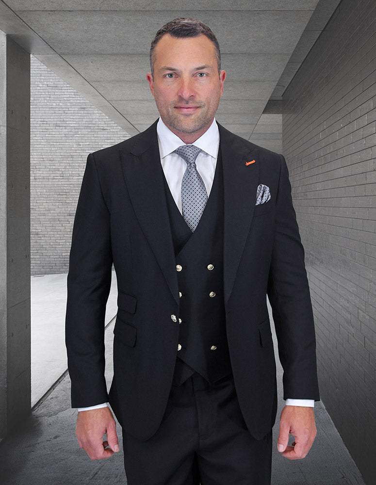 A man wearing the STATEMENT CLOTHING | AMIRI-BLACK suit, white shirt, and patterned tie from Statement Clothing stands in a sleek gray concrete hallway.