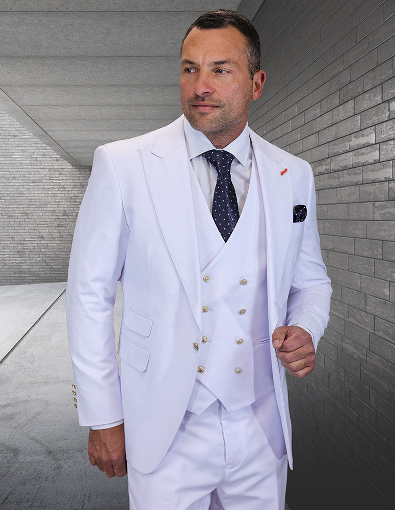 A man in the STATEMENT CLOTHING | AMIRI-WHITE suit by Statement Clothing, paired with a white shirt and dark polka-dot tie, stands outdoors against a gray brick wall.