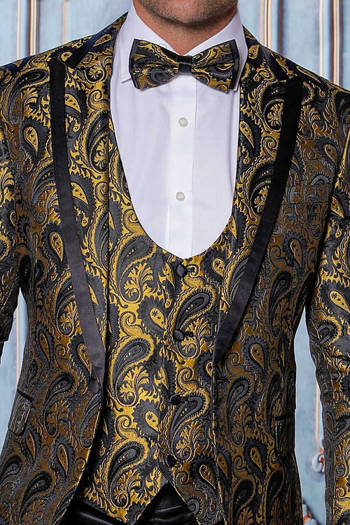 A man models the Insomnia MANZINI ASHER 3-Piece Slim Fit Shiny Satin Paisley Gold Tuxedo Prom Suit with a matching bow tie, standing against an ornate blue backdrop to highlight its intricate design.
