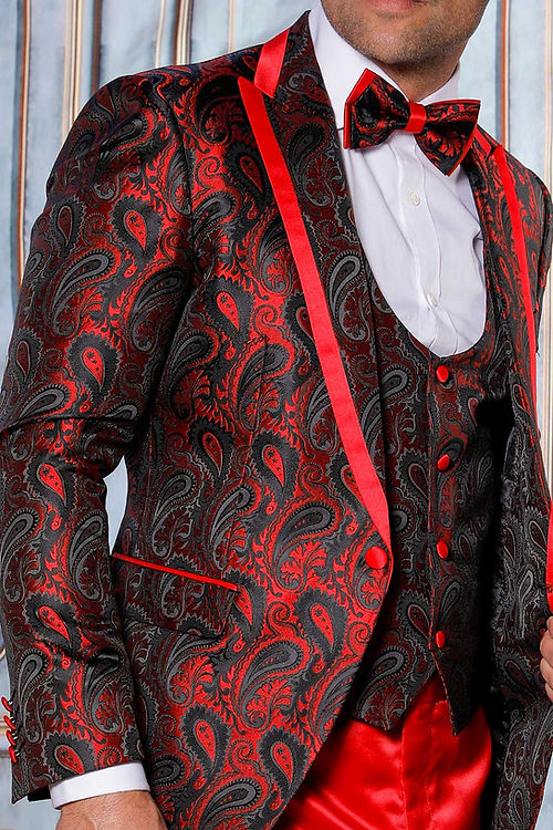 A man poses against an ornate backdrop in the Insomnia MANZINI ASHER 3-Piece Slim Fit Shiny Satin Paisley Red Tuxedo Prom Suit, accompanied by a matching bow tie and red trousers.