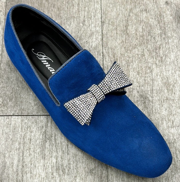The "Exclusive Formal Dress Shoe Blue FOWLER" by UNIQUE DESIGN MENSWEAR, adorned with a rhinestone bow on top, exudes Italian craftsmanship as it is elegantly displayed on a gray wooden floor.