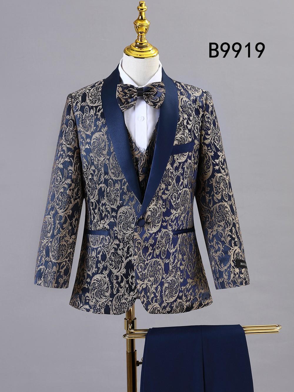 The BOY SUIT 5-PC SET B9919 by Unique Design Menswear features a navy blue and gold paisley pattern with vest and bow tie, shown on a mannequin with navy formal pants—a standout in boys' formal wear.