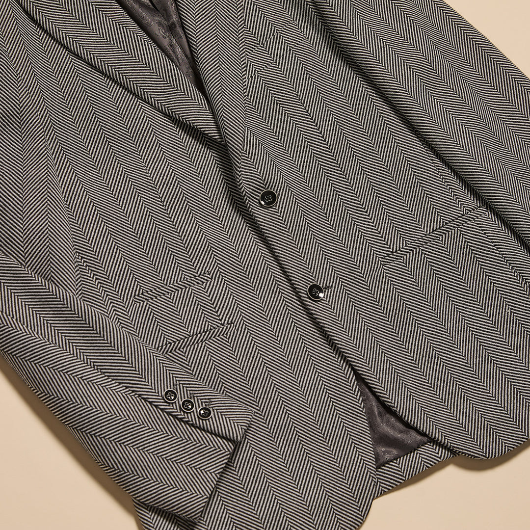 A man wearing the Inserch Herringbone Blazer BL273-00041 in Black/White by Inserch with a black turtleneck poses against a beige background, one hand in his pocket.