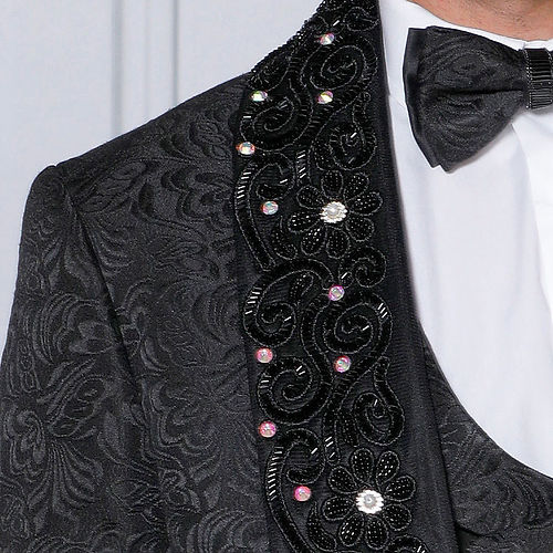 A man in an Insomnia MANZINI DIOR 3-Piece Slim Fit Rhinestone & Bead Trim Floral Black Tuxedo Suit with embellished lapels, elegantly wearing a bow tie, stands against a light-colored background.