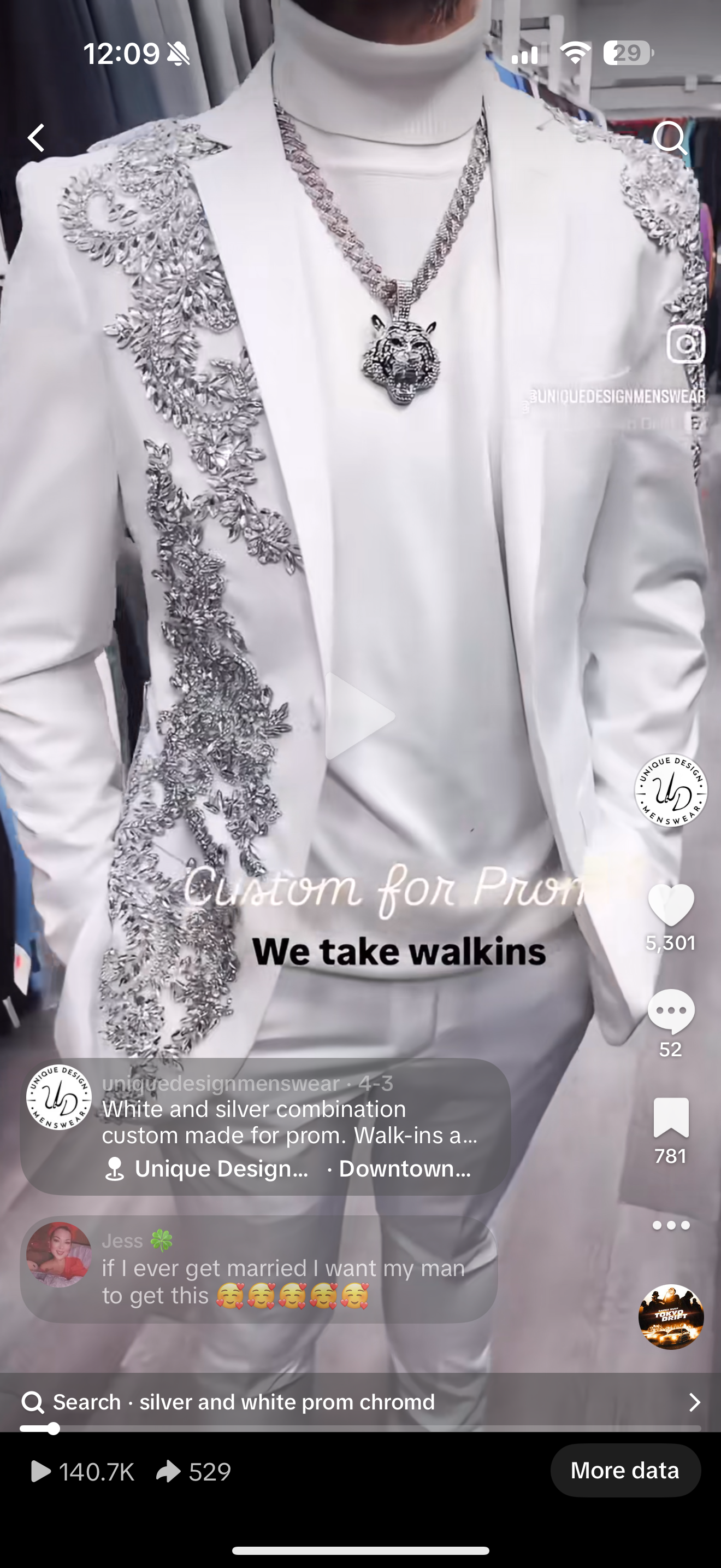 A young man stands against a plain background, wearing the Unique Design Menswear Custom Prom Suit White with Silver Rhinestones, paired with a white turtleneck and a silver chain necklace.