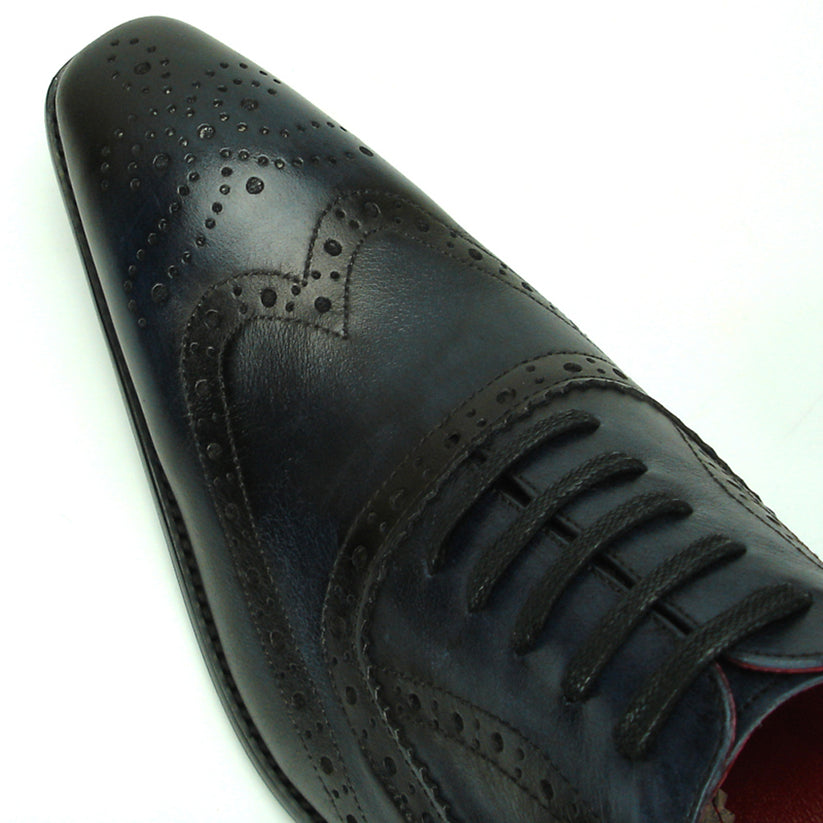 The FI-8710 Black Wing Tip Encore by Fiesso, a men’s fashion shoe in black and navy blue crafted from leather with decorative perforations, black laces, and a low heel, is displayed on a white background.