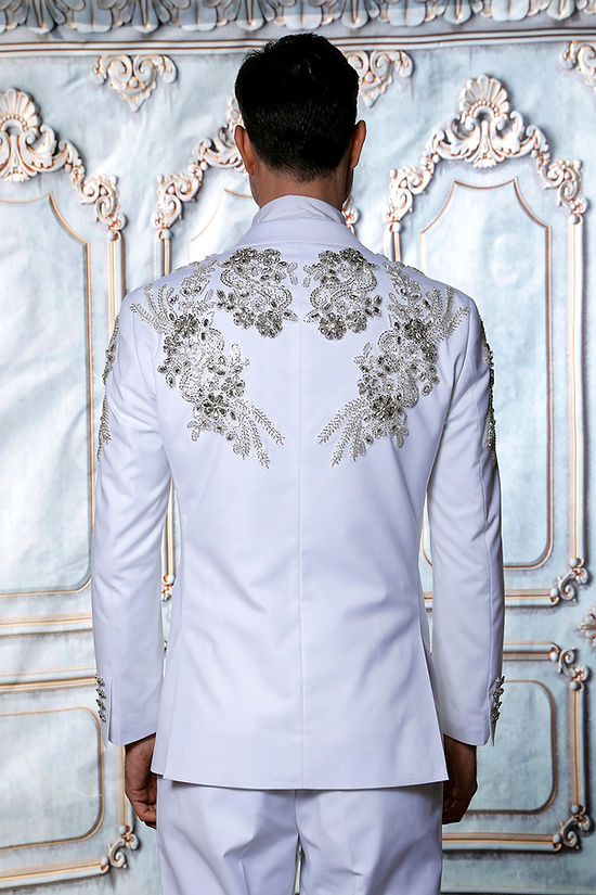 A man in an Insomnia MANZINI GQ300 2-Piece Slim Fit Rhinestone Pattern Double Breast White Tuxedo Suit stands against a decorative backdrop.