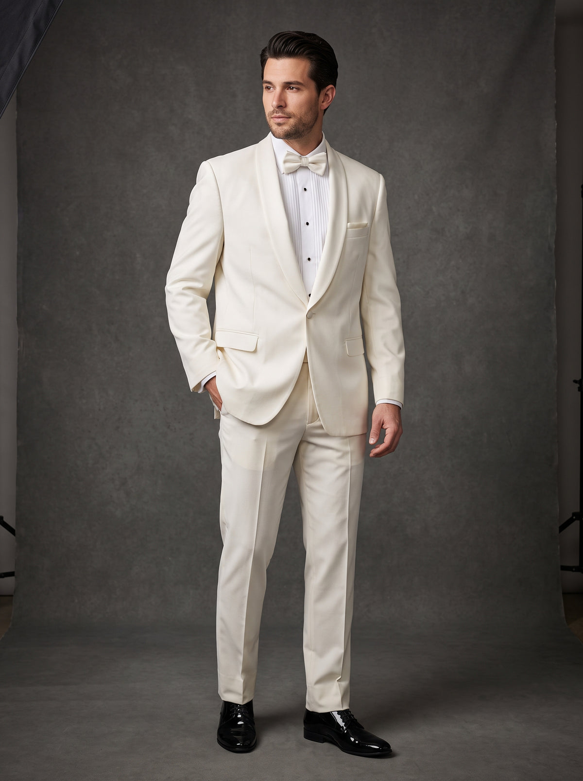 A man wearing an off-white BOLZANO Shawl Collar Blazer with a shawl collar, white shirt, and matching bowtie, paired with black dress shoes for a classic formal look.