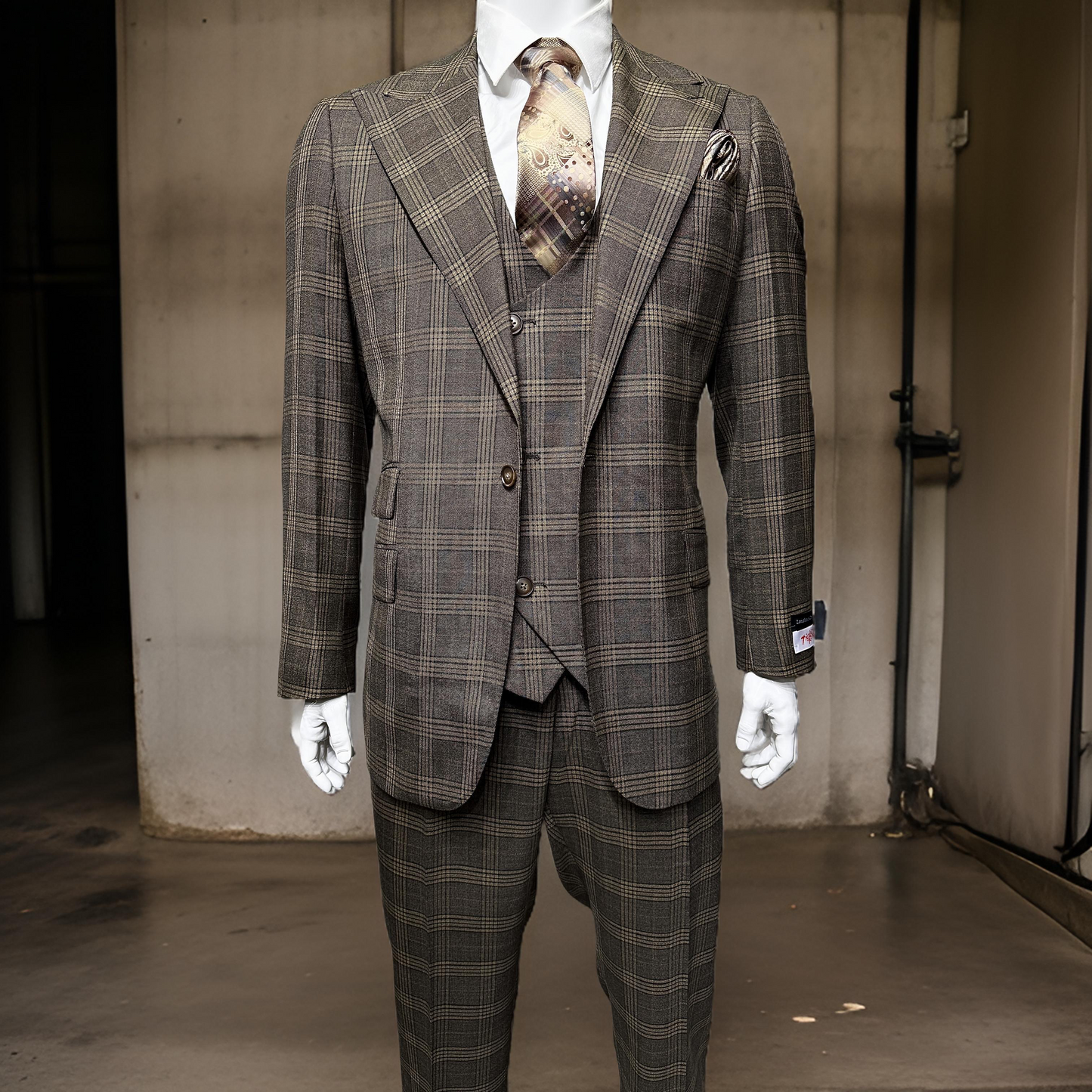 A mannequin showcases the Tiglio Rosso Orvietto Brown Plaid TL7525 suit, available in select sizes, paired with a patterned tie against an industrial concrete backdrop.