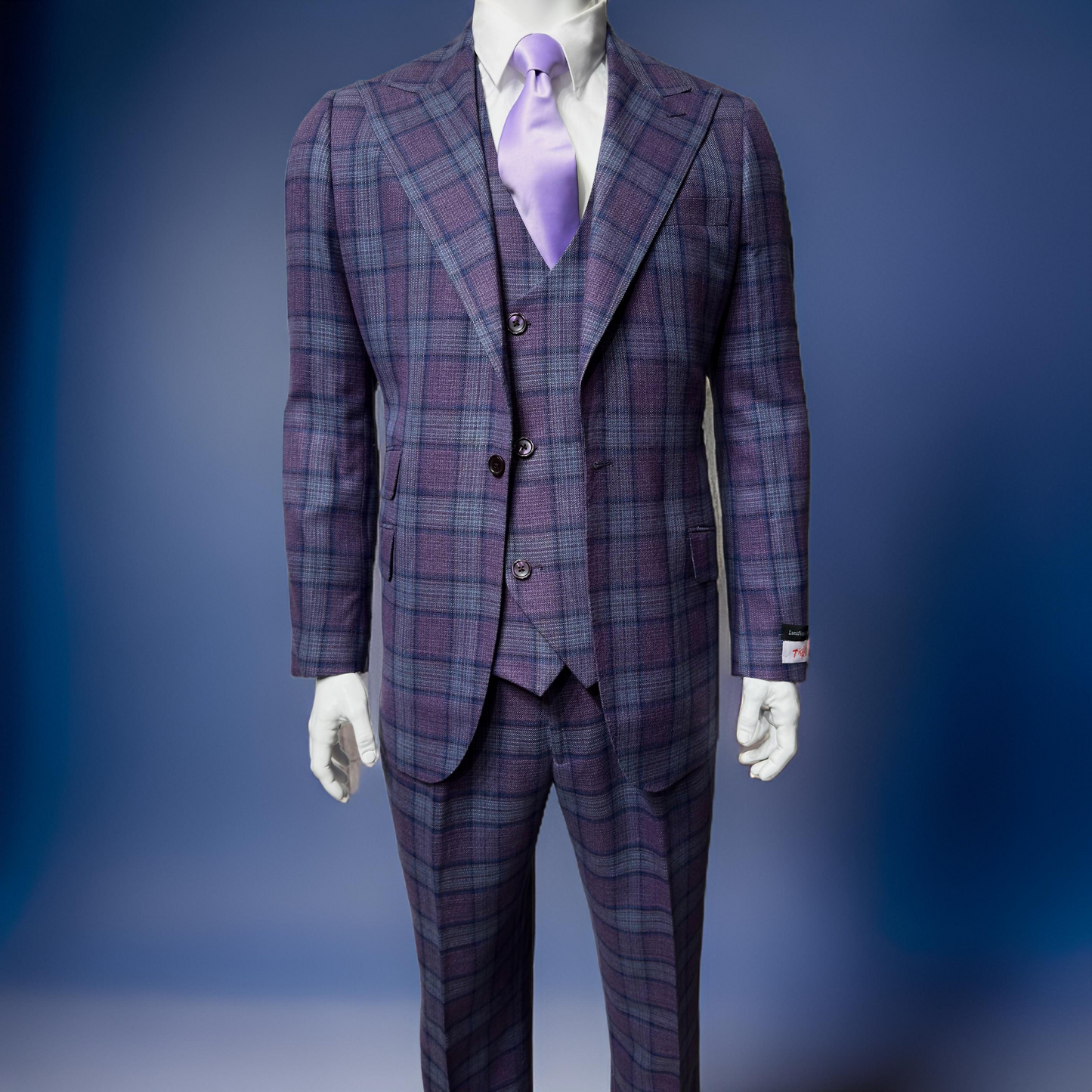 A mannequin wears the Tiglio Rosso Orvietto Lilac/Blue TL7510 suit with a matching vest and lavender tie by Tiglio Rosso, set against a blue background. Available in sizes 40R, 44R, 50R, 52R, 56R, 44L, and 52L.