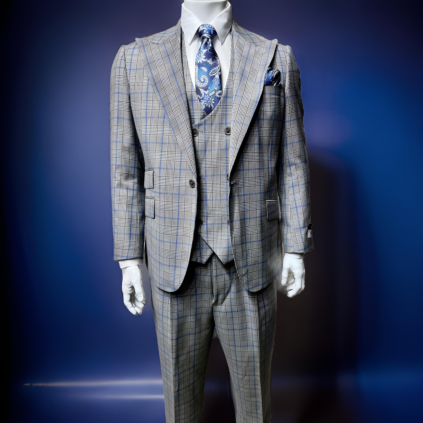 A mannequin displays a Tiglio Rosso Orvietto Grey/Blue Plaid TL6350 suit, paired with a blue paisley tie and pocket square. Made from 100% wool, the ensemble stands elegantly against a dark blue background.