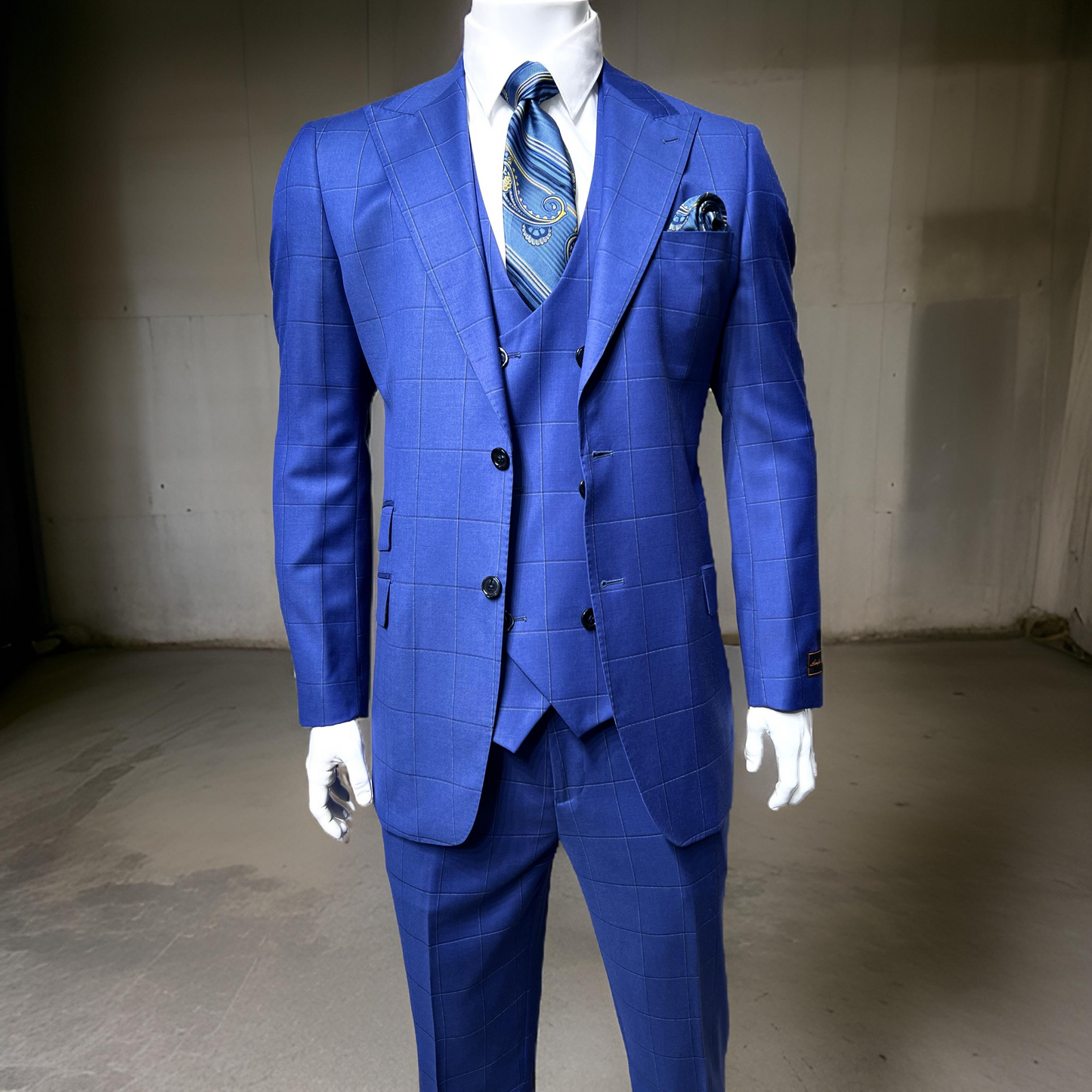 A mannequin showcases the Tiglio Luxe Prosecco Modern Fit pure wool suit & vest in blue windowpane (48R, 44L), an elegant nod to classic European styling, displayed indoors with a matching tie and pocket square.