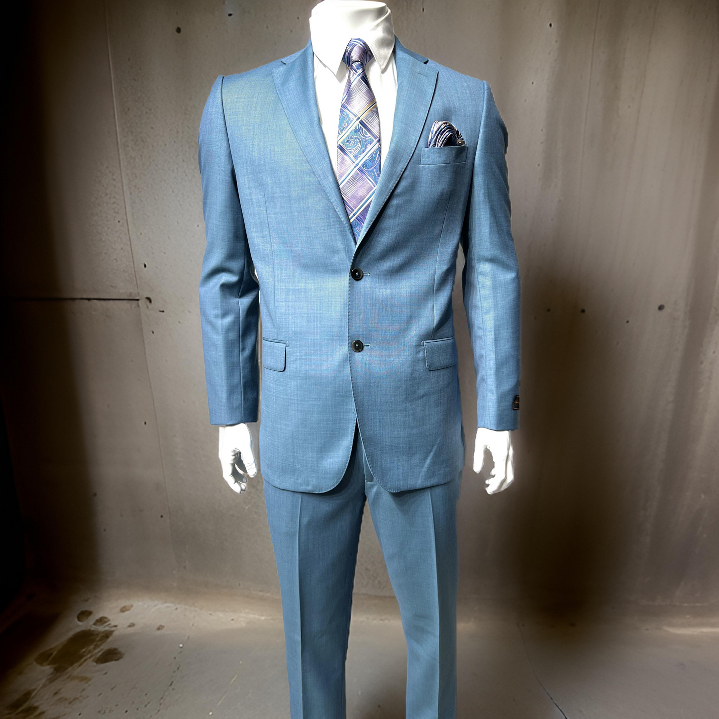 A mannequin dressed in the Tiglio Luxe Dolcetto Modern Fit Teal Suit TL2538, crafted from pure wool and complemented by a patterned tie and pocket square, stands elegantly in front of a gray backdrop.