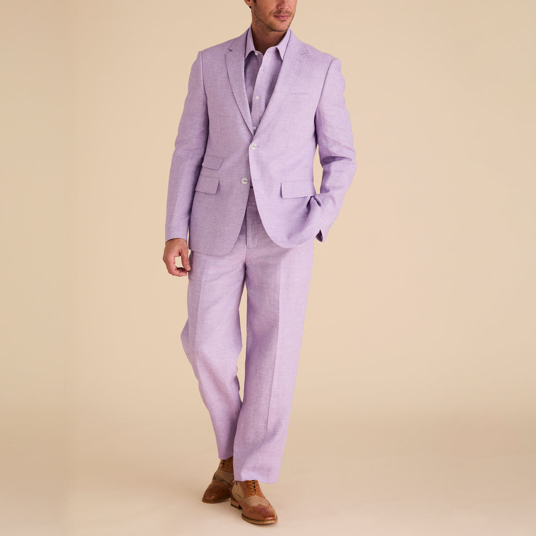 A man wearing the Inserch Slim Linen Blazer SU880-00119 in lavender, paired with a matching shirt and brown dress shoes, stands against a beige background.