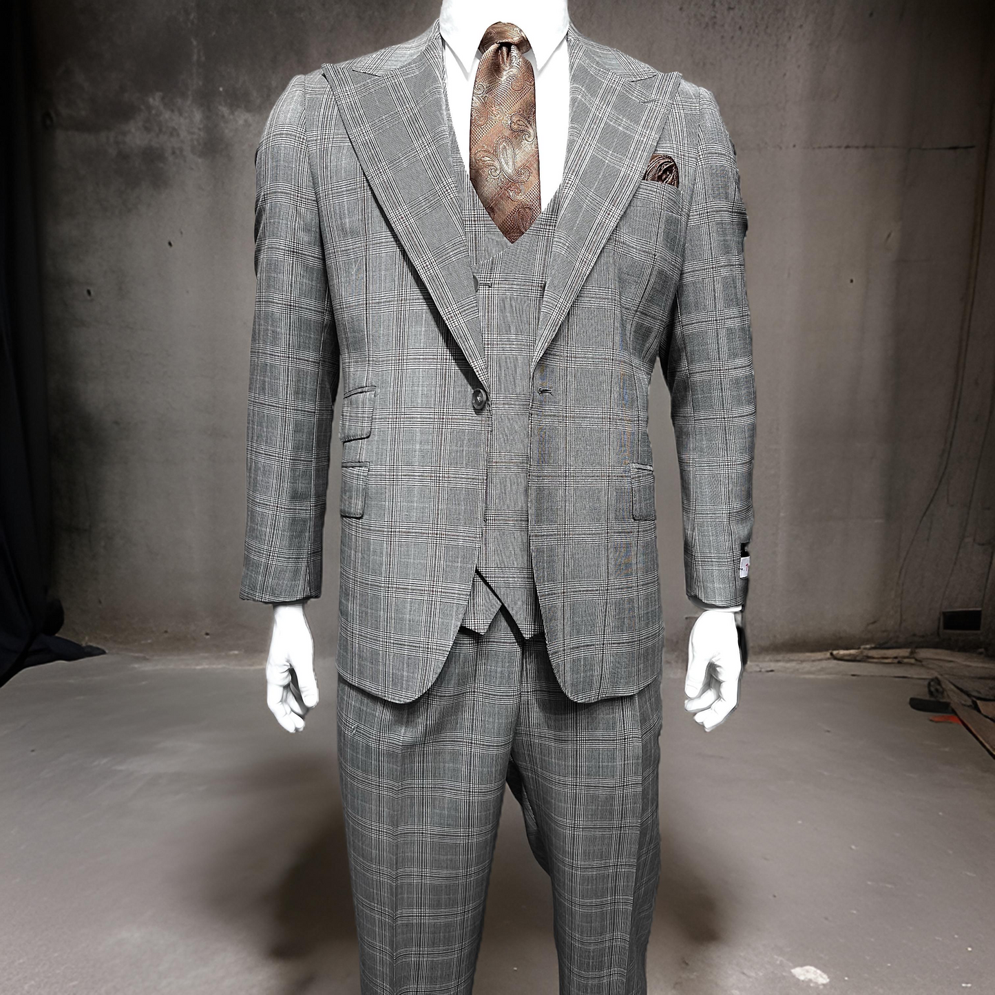 A Tiglio Rosso Orvietto Taupe/Brown Plaid TL5203 suit is shown on a mannequin with a brown patterned tie against a plain, industrial-style background.