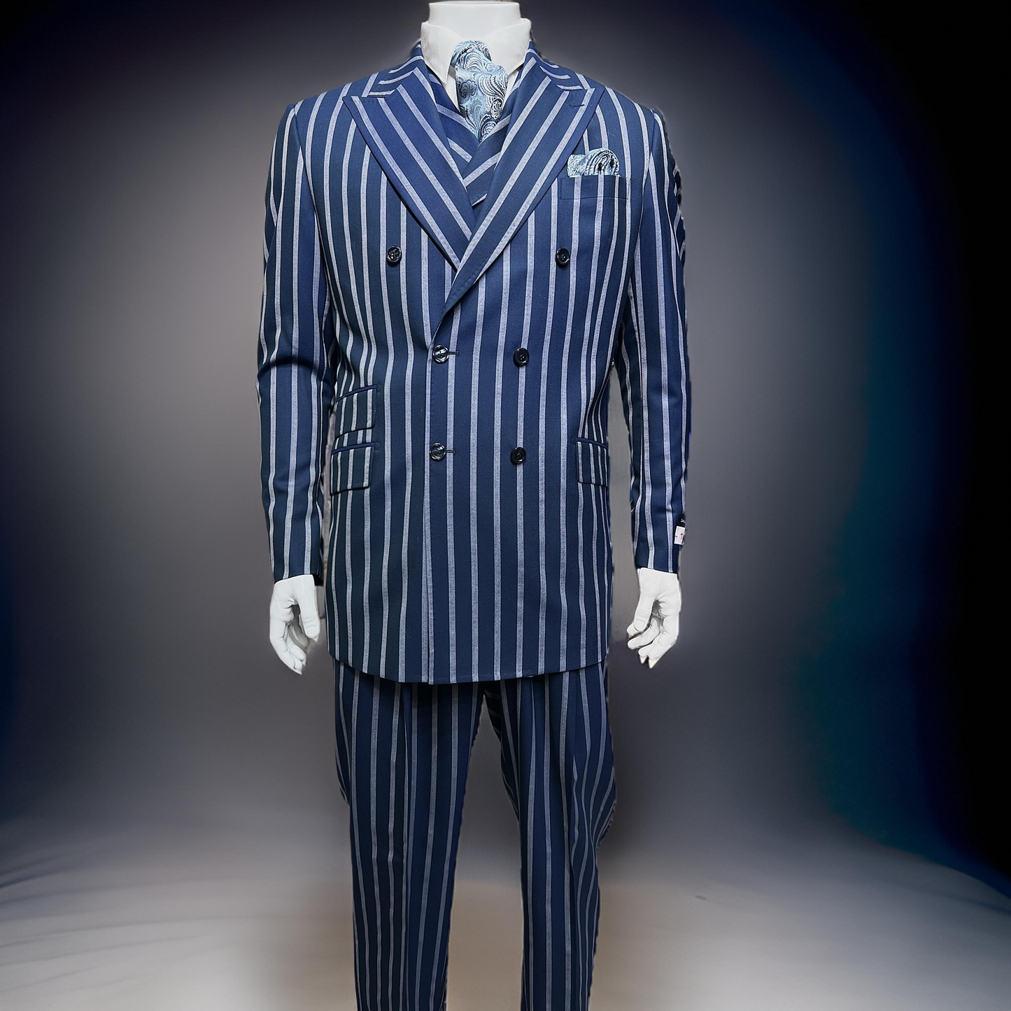 A mannequin wears a Tiglio Rosso DB Este Blue/Grey Bold Stripe suit (TL4122), paired with a matching vest, white shirt, and patterned tie, set against a dark gradient background. Sizes: 48R, 50R, 52R, 46L, 50L, 54L.