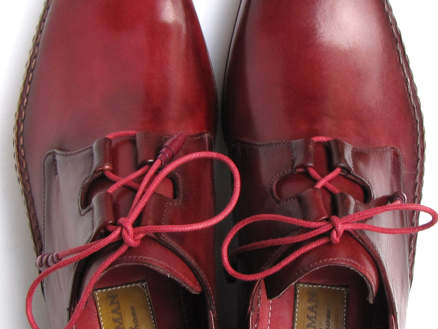 A pair of Paul Parkman Ghillie Lacing Handsewn Shoes in burgundy (022-BUR), featuring red laces, is displayed overlapping on a white background.