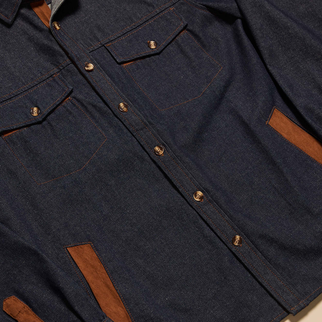 A man stands against a beige background wearing the Inserch Denim Shirt Jacket with Suede Trim 2pc Set (JS005-P005-00195 Indigo) by Inserch, styled with an orange sweater and dark brown shoes.