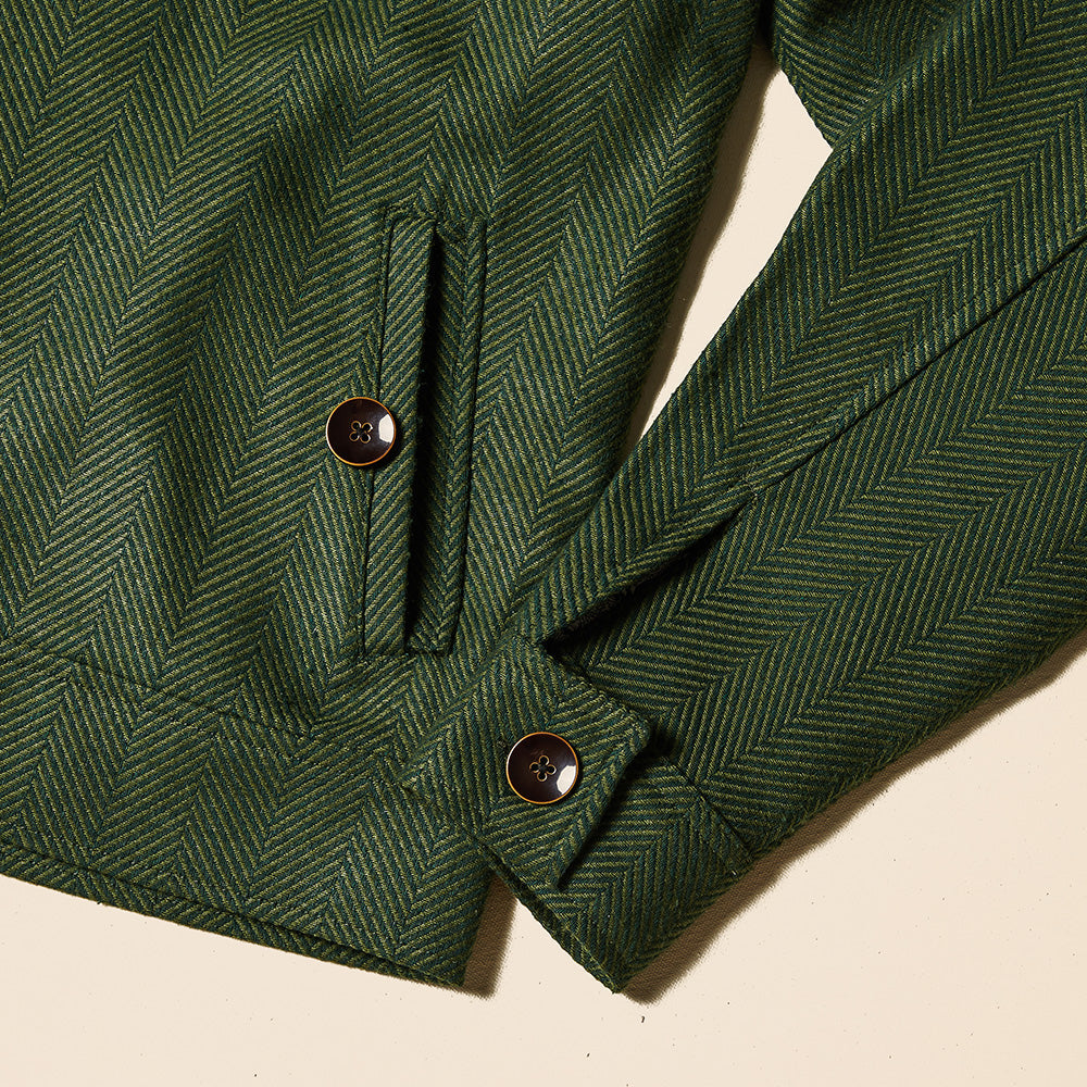 A man wears the Inserch Wool Blend Herringbone Jacket JS263-19 Olive with matching pants, a tan sweater, and white sneakers, standing against a plain beige background.