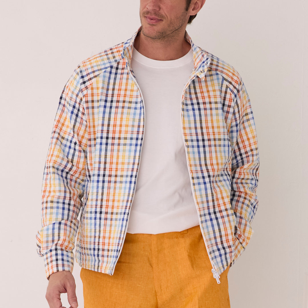 A man in an Inserch Seersucker Check Jacket JS271-00056 White Multi, featuring a classic collar, stylishly pairs it with a white t-shirt and bold orange pants against a plain white background.