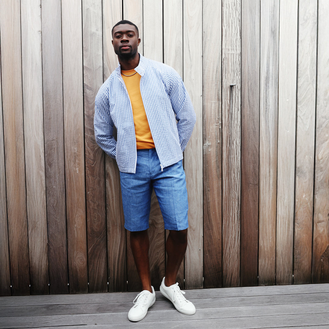 A person sports the Inserch Seersucker Stripe Jacket JS506-00101 in True Blue over a dark shirt, paired stylishly with white shorts and sneakers. They are set against a simple white background.