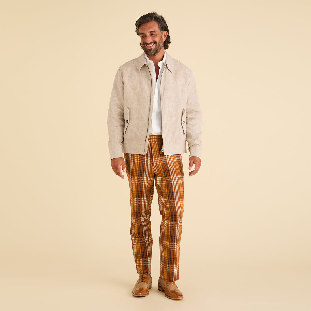 A man stands smiling, wearing an Inserch Linen Harrington Jacket (JS661-00006 Oatmeal) with a metal zipper, a white shirt, orange plaid pants, and brown shoes against a plain light background.