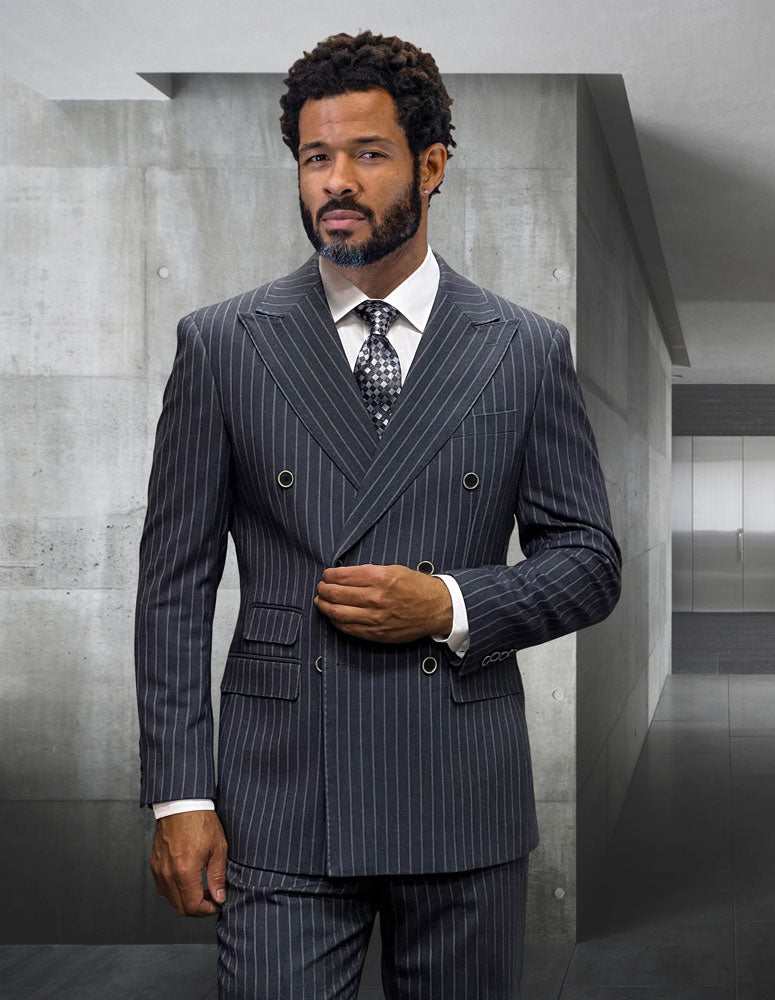 A bearded man with curly hair wears the Statement Clothing KELLY-CHARCOAL suit, featuring a modern fit pinstripe design, paired with a white shirt and patterned tie, standing in a minimalist hallway.