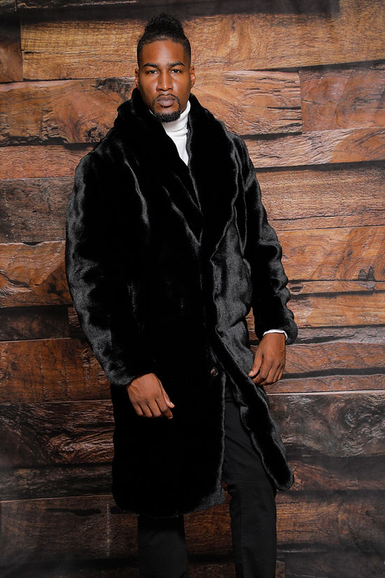 Wearing the Insomnia MANZINI MZW-323 Black 3/4 Faux Fur Winter Coat, the person stands elegantly against a wooden wall backdrop.