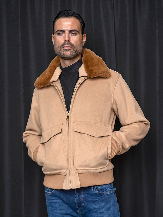 Man wearing a Manzini MZW-501 Camel Bomber Jacket Coat with removable faux fur collar, black long sleeve shirt, and blue jeans, standing in front of a black curtain backdrop.