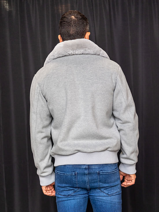 A person stands against a black curtain, wearing the Insomnia MANZINI MZW-501 Grey Bomber Jacket Coat with a removable faux fur collar, paired perfectly with blue jeans for a stylish yet versatile look.