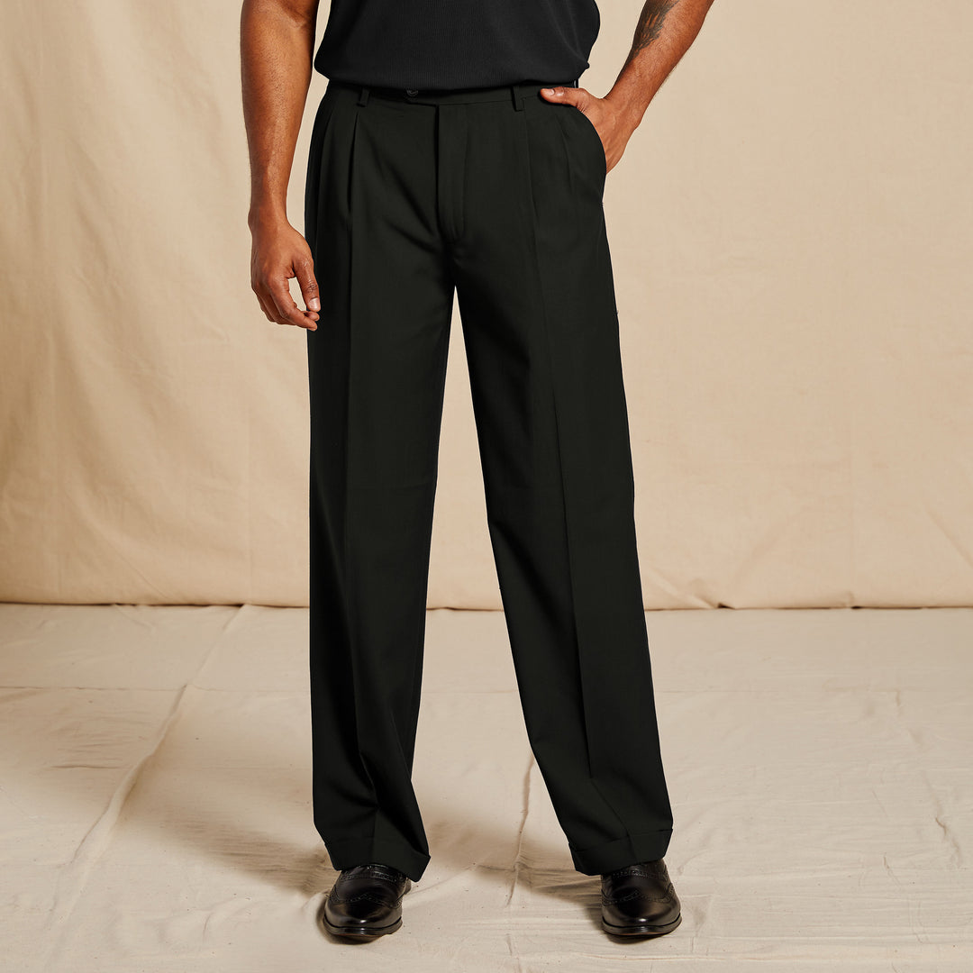 A person wearing Inserch Regular Fit Two Pleat Pants P1199S-01 Black, a black shirt, and black shoes stands on a light-colored floor against a neutral backdrop.