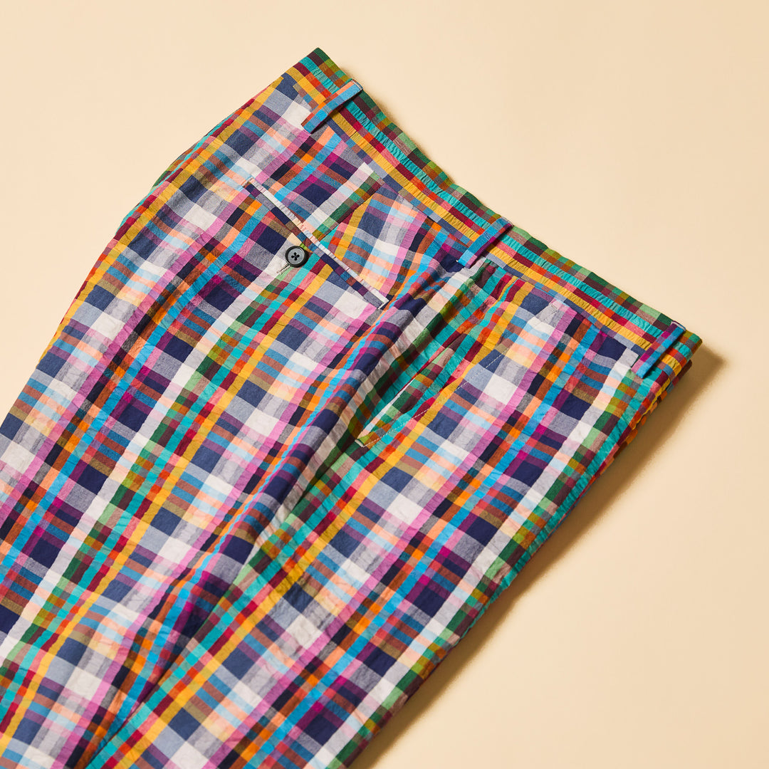 A person wears Inserch Seersucker Plaid Pants P276-00066 Multicolor, crafted from premium cotton. In a neutral-colored room, only their lower half is visible, highlighting the modern fit of these vibrant pants paired with a white shirt.