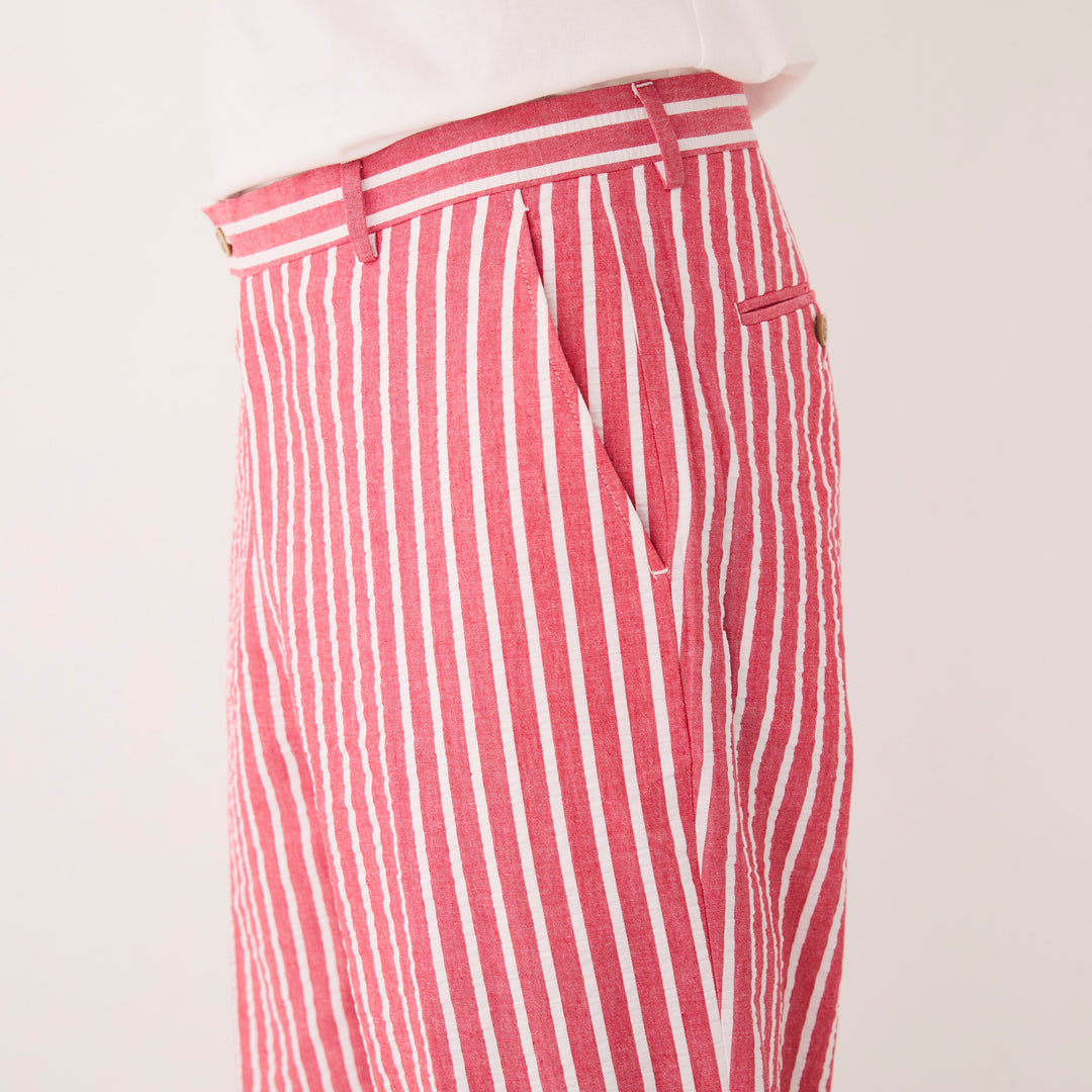 A person stands against a plain beige background, wearing the Inserch Seersucker Wide Stripe Blazer BL507-00030 in red with a crisp white shirt and brown shoes, subtly complemented by gingham check accents.