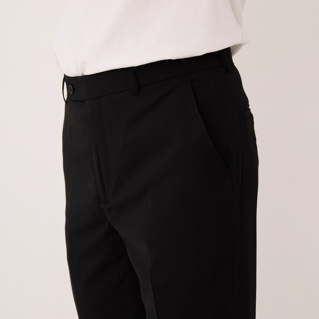 Model wearing Inserch Crepe Flat Front Pants P9356-00001 Black by Inserch, paired with a white shirt. Shown from mid-torso to thigh, with one hand in the pants pocket.