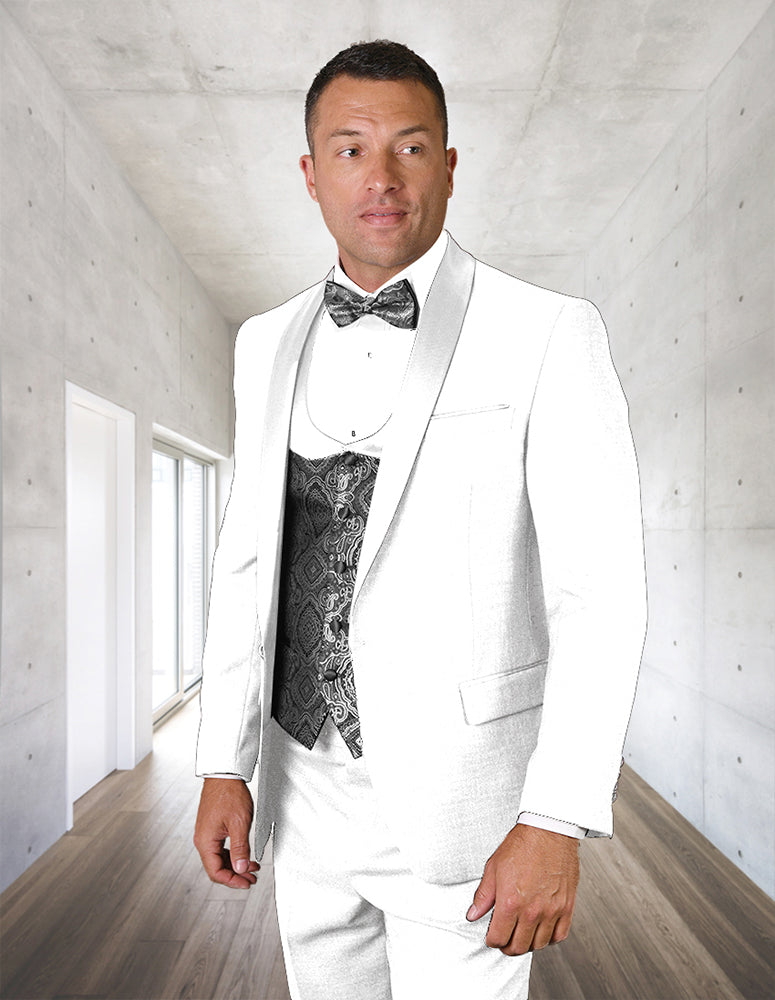 A man in the STATEMENT CLOTHING | PALMERO-WHITE tuxedo by Statement Clothing stands in a modern minimalist hallway, showcasing flat front pants, a white suit jacket, and a patterned black vest with bow tie.