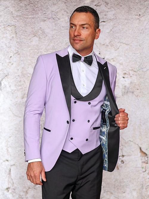Wearing a MANZINI ROME Slim Fit 3-Piece Stretch Spandex Lavender Tuxedo Suit by Insomnia, which features patterned lining and black lapels, a man stands confidently against a textured light background.