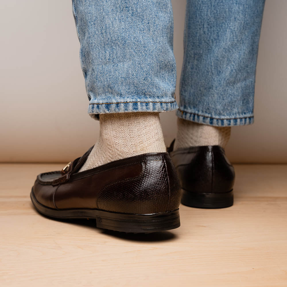 The Marco Di Milano Ravello Brown loafers, crafted from genuine lizard with a metal buckle, are showcased with one shoe upright and the other on its side to highlight the elegant hand-painted finish.